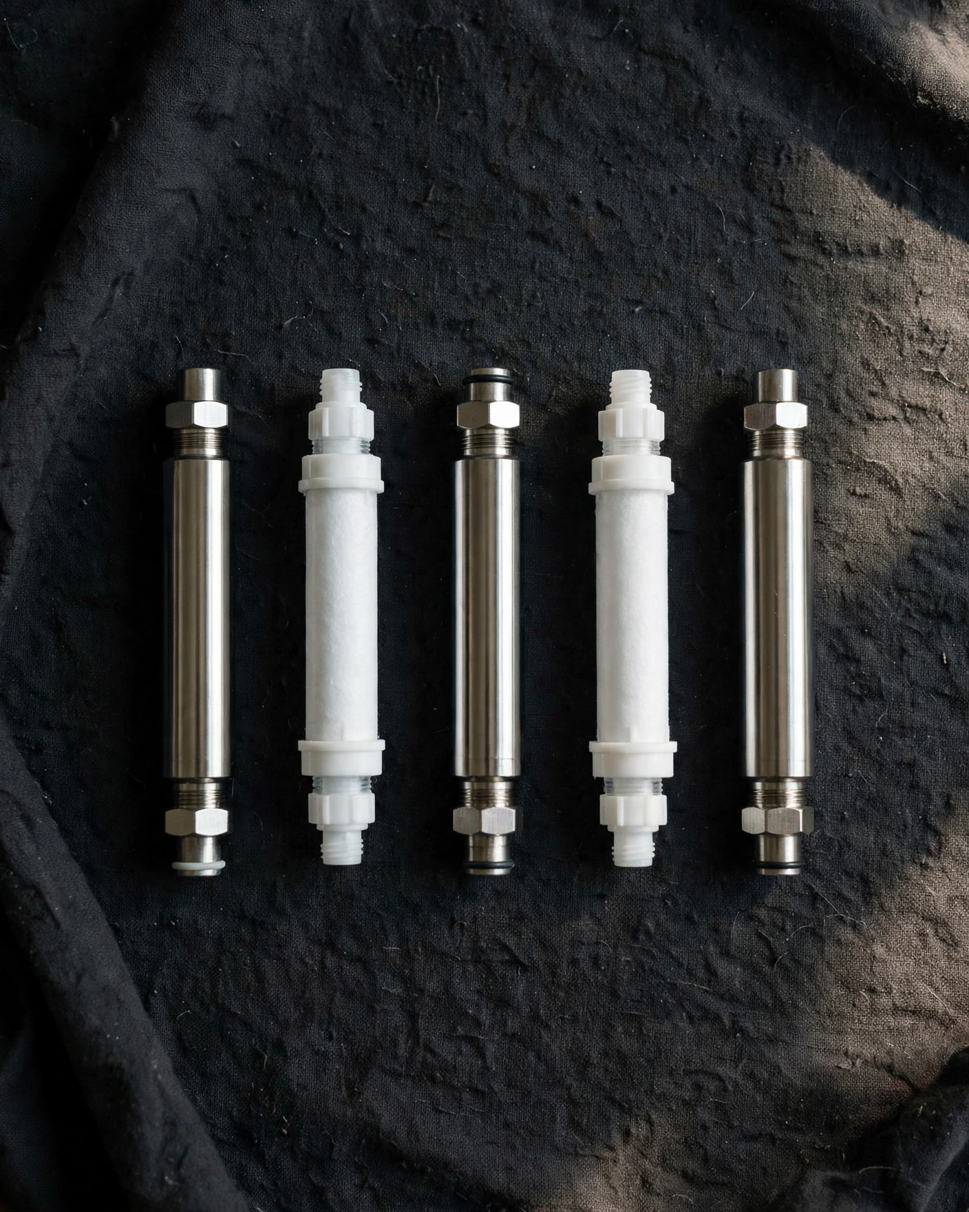 Inline shower-style filter cartridges arranged in a flat-lay on a dark workbench cloth, workshop mood
