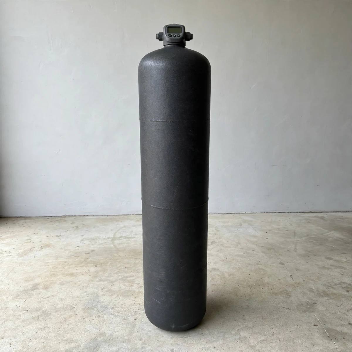 Dark charcoal SpringWell-style whole-house media filter tank with a digital control head against a light grey wall